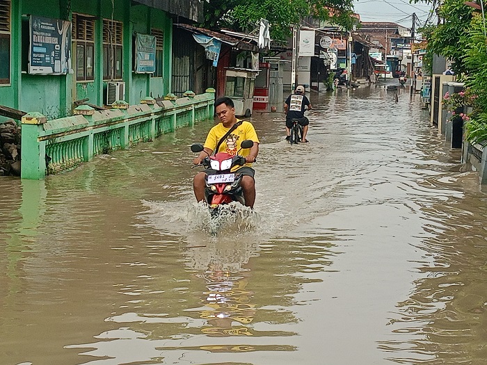 Warga berusaha melintasi jalanan yang tergenang air akibat luapan Sungai Kendal di kawasan permukiman padat penduduk
