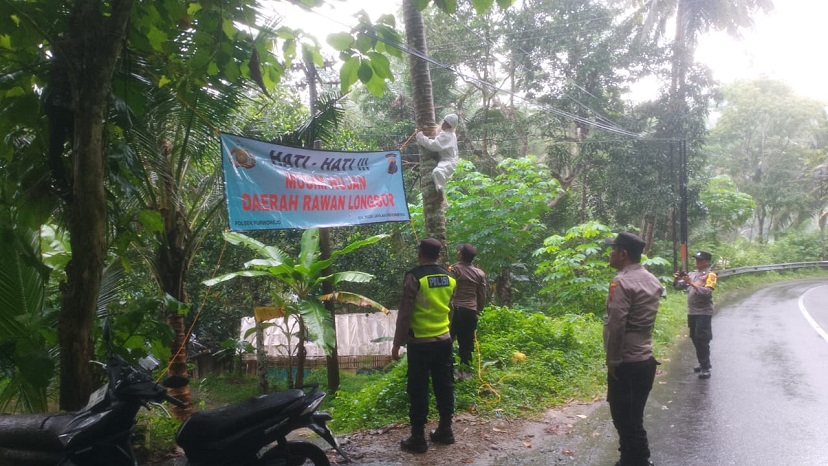 Anggota Polsek Purworejo sedang memasang banner imbauan rawan longsor di pinggir jalan desa