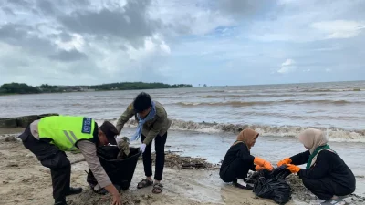 Alat berat loader sedang mengeruk tumpukan sampah kayu dan plastik di bibir Pantai Teluk Awur Jepara.