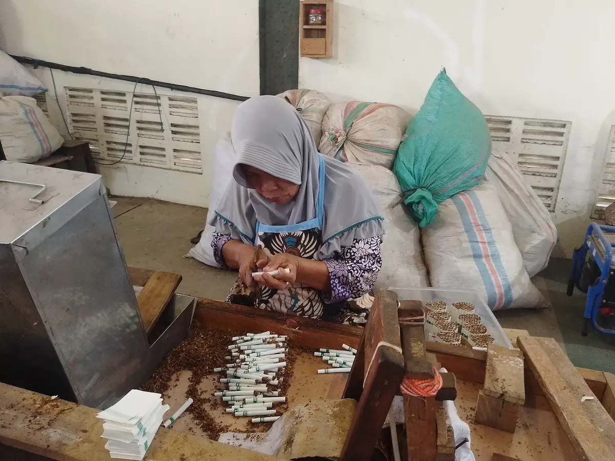 Seorang buruh rokok perempuan di Kudus tampak fokus melinting tembakau di pabrik.