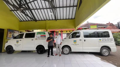 Kades Dersalam Kudus M Sulaiman berdiri di depan armada layanan ambulans gratis yang siap melayani kondisi darurat warga selama 24 jam.