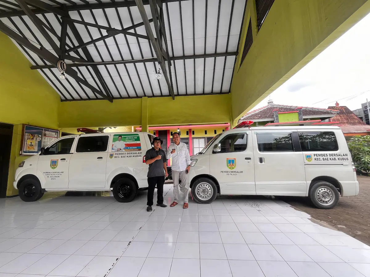 Kades Dersalam Kudus M Sulaiman berdiri di depan armada layanan ambulans gratis yang siap melayani kondisi darurat warga selama 24 jam.