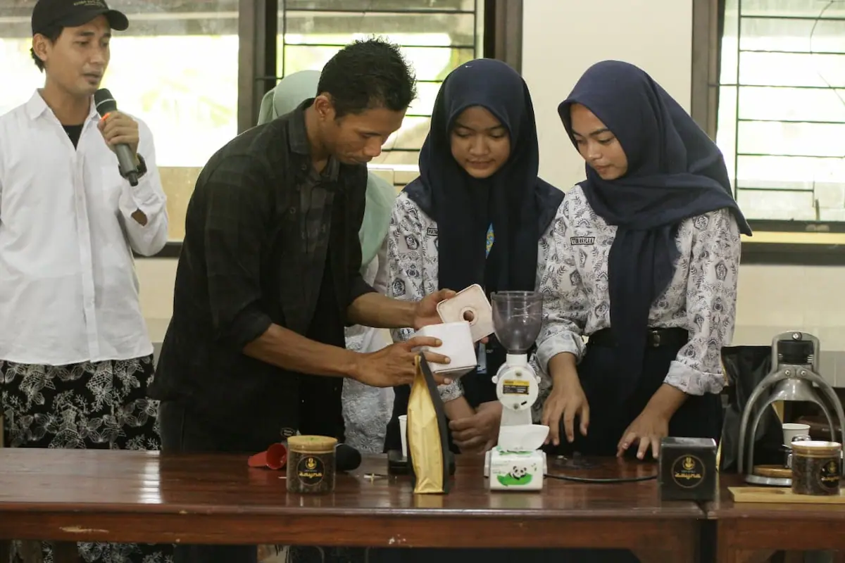 Siswa SMP 3 Dawe sedang belajar menggunakan mesin penggiling kopi didampingi instruktur.