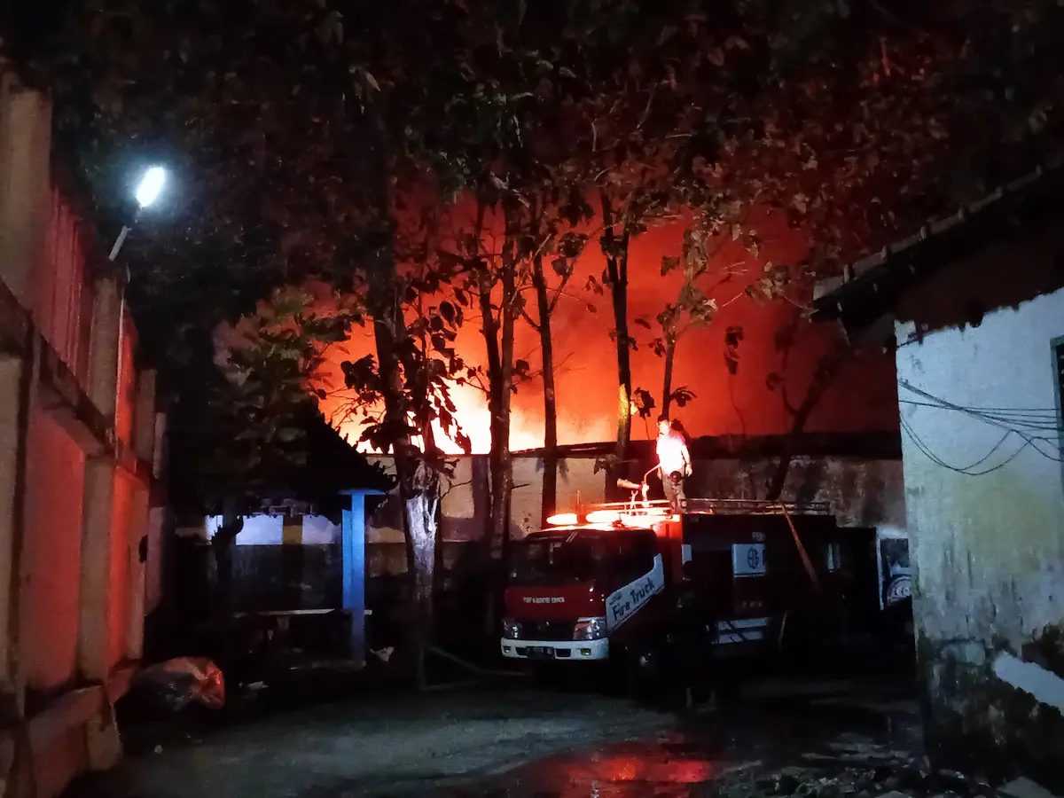 Petugas pemadam kebakaran menyemprotkan air ke arah bangunan gudang busa PT Chenqi Industrial Indonesia yang terbakar hebat di malam hari.