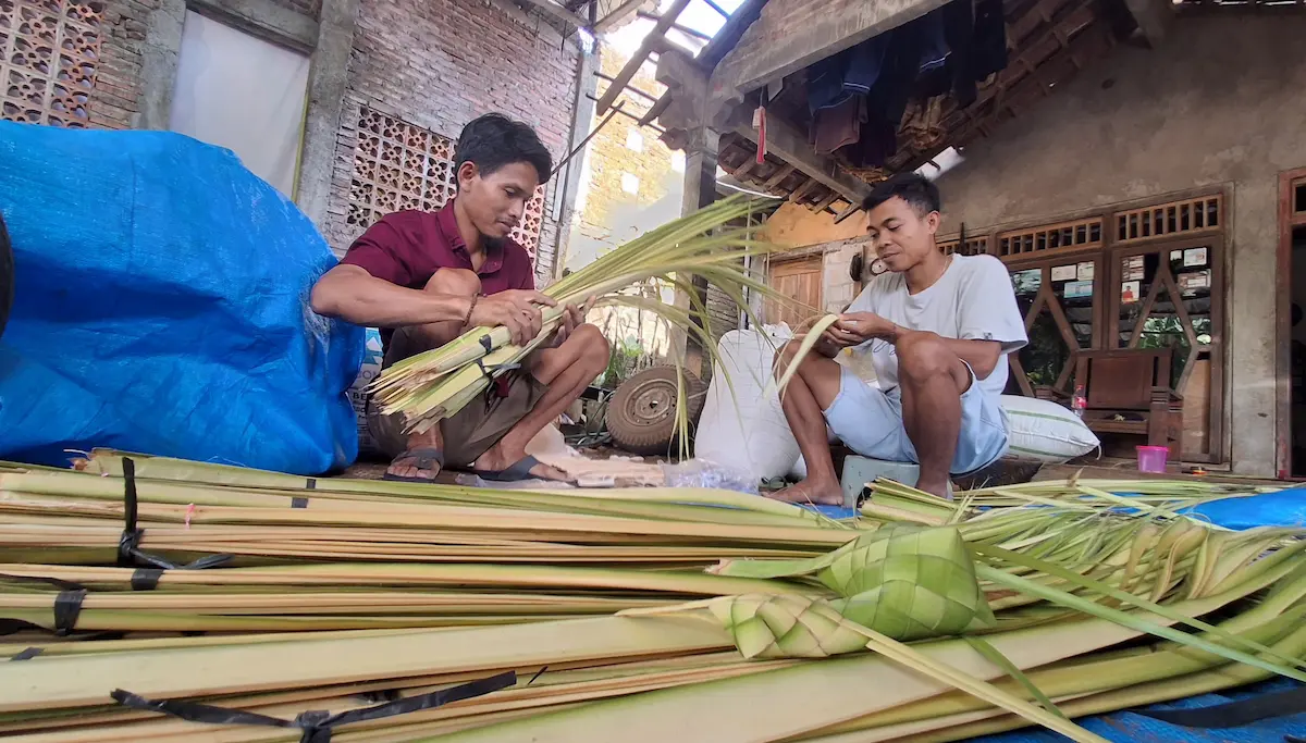 Seorang pria pedagang asal Jepara sedang merapikan tumpukan daun janur dan ketupat untuk dijual menjelang perayaan tradisi Bodo Kupat.