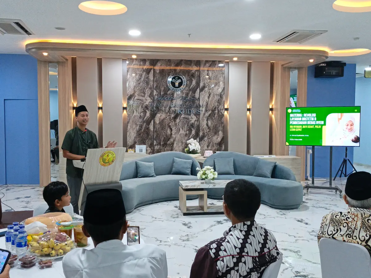 Direktur RSI Sunan Kudus Ahmad Syarifudin berdiri memberikan presentasi tentang inovasi layanan Materna untuk ibu hamil di depan layar proyektor.