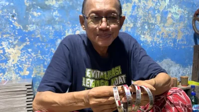 Subandi, seorang perajin monel di Jepara, sedang memegang produk gelang identitas haji di tempat usahanya.