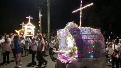 Ribuan jemaat gereja berjalan beriringan membawa obor dan lilin menyusuri jalan desa pada malam hari yang gelap.